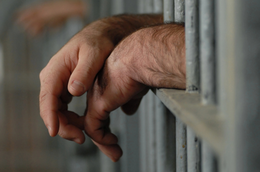 Mans hands behind bars in jail.