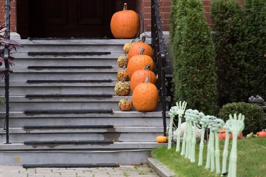 Pumpkins and plastic skeleton hands decorate a doorstep on Halloween.