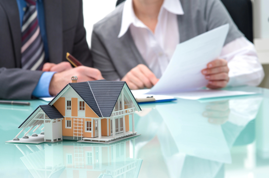 People handling real estate paperwork, with a model of a house.