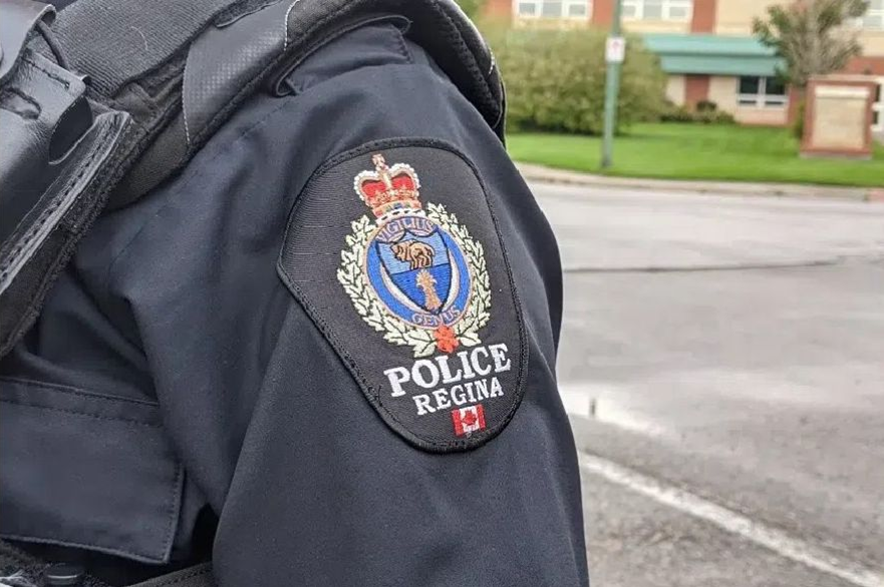A Regina police officer standing on the street with their uniform shoulder patch visible.