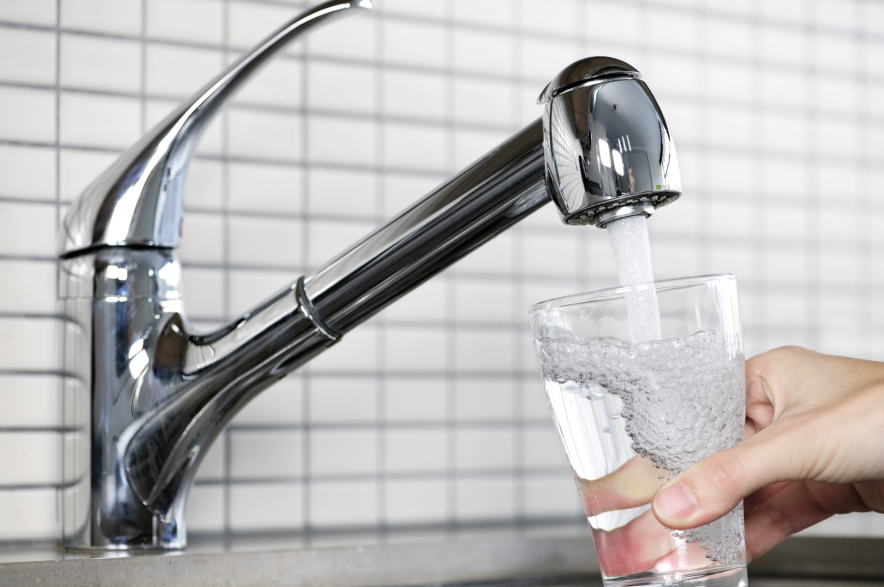 A person pours a glass of water out of a kitchen faucet.