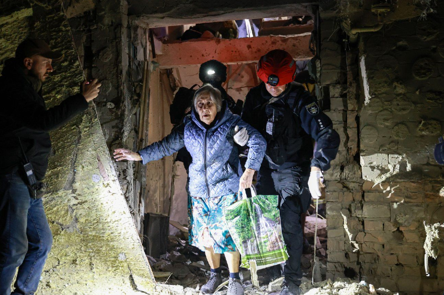 A policeman helps an elderly woman to walk out from a residential building damaged by a Russian airstrike in Zaporizhzhia.
