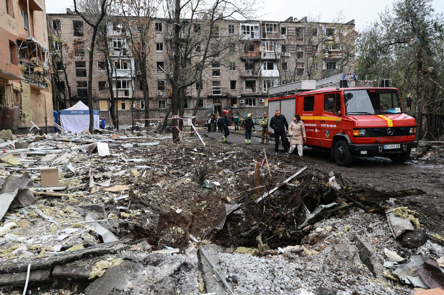 People walk past a crater in front of a residential building damaged by a Russian airstrike in Zaporizhzhia.