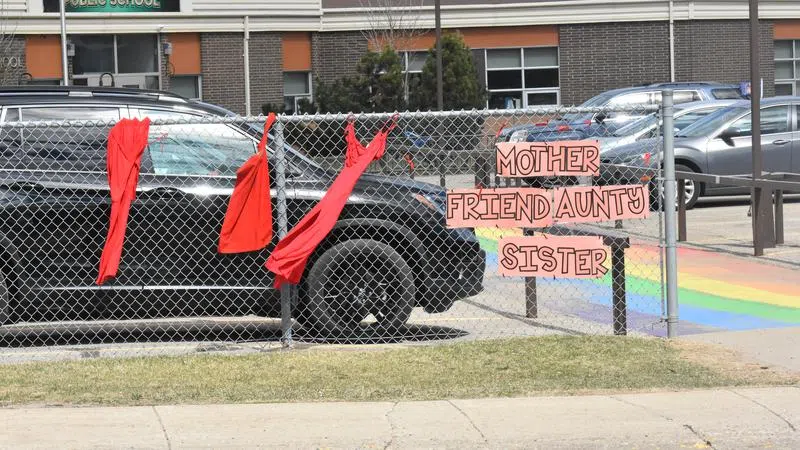 Red dresses, red ribbons, and various words to describe a woman in front of John Diefenbaker School. (Logan Lehmann/paNOW Staff)