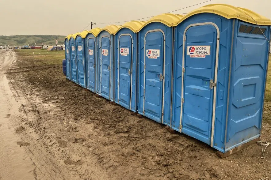 A row of blue porta-potties with yellow roofs sit on the side of a muddy road.
