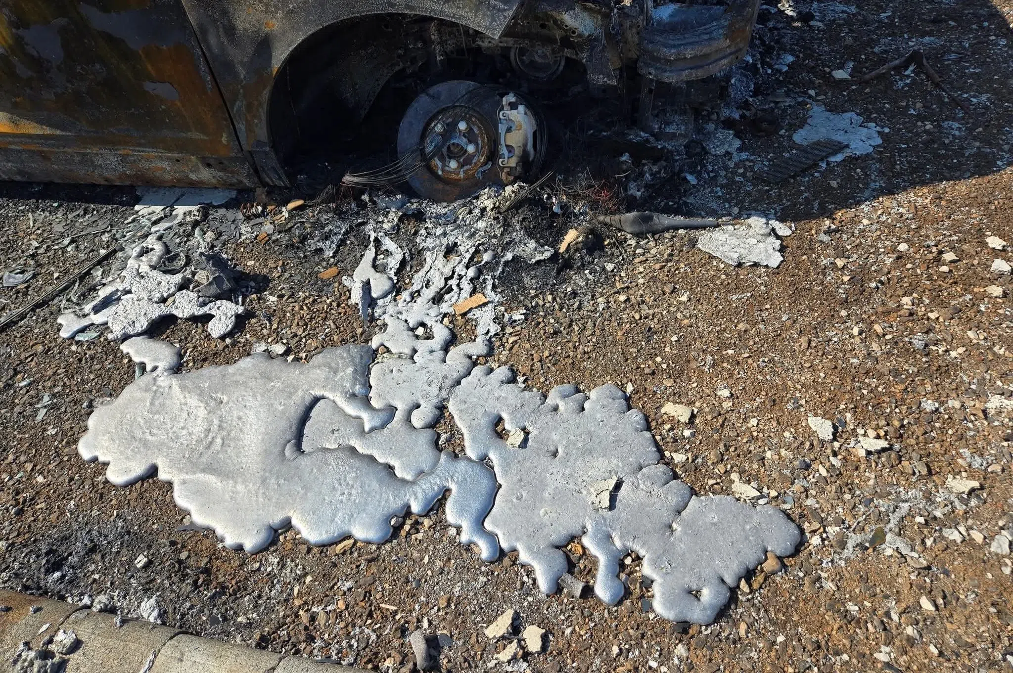 Silver liquid lies in front of a burnt car