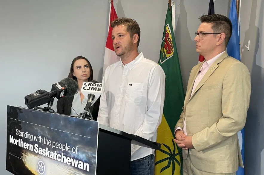 A man in a white collared shirt stands behind a podium with a woman to the left and a man to the right