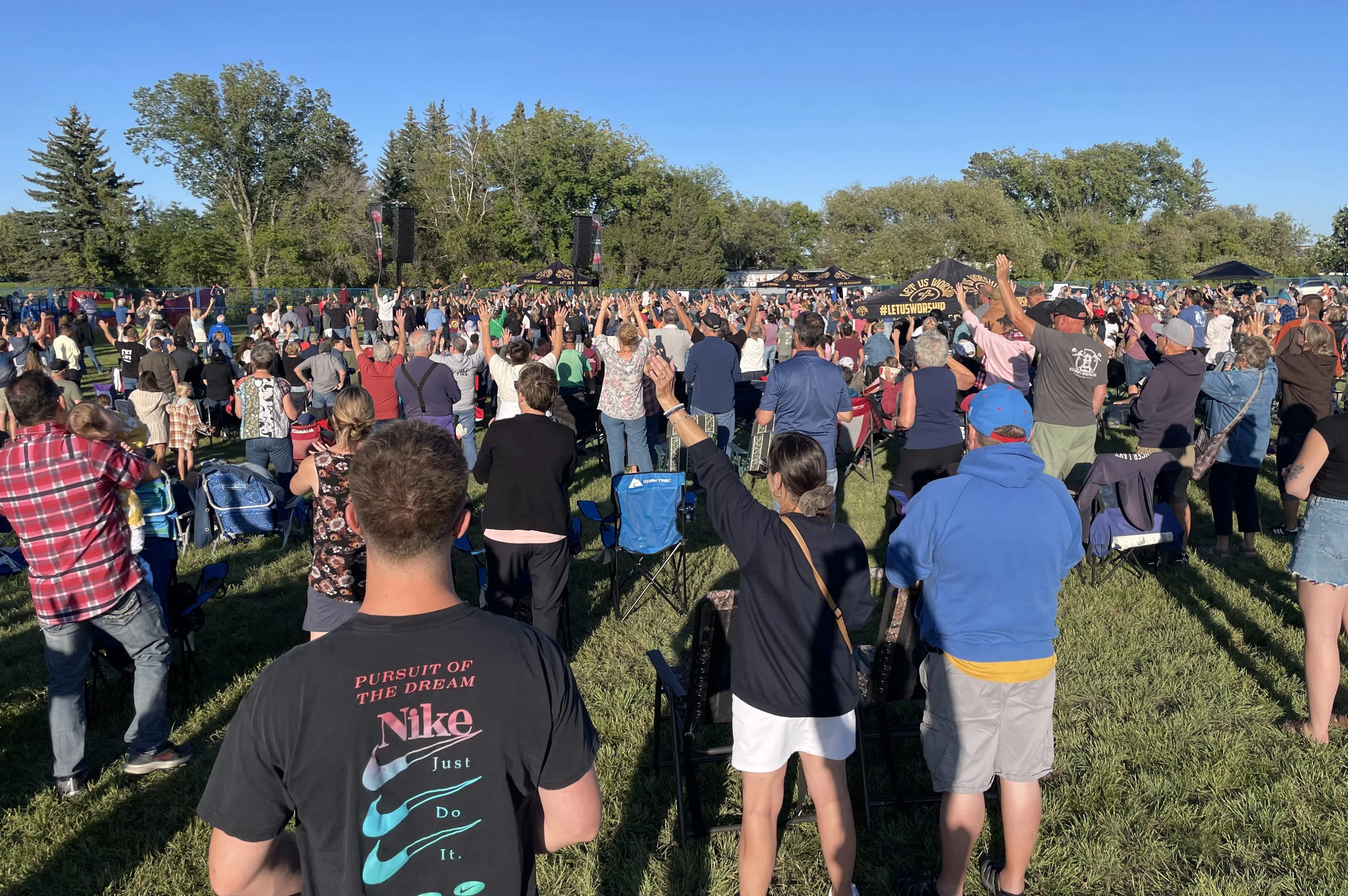 Thousands of concertgoers stand in a field, with blue sky, some holding up their hands for Sean Feucht