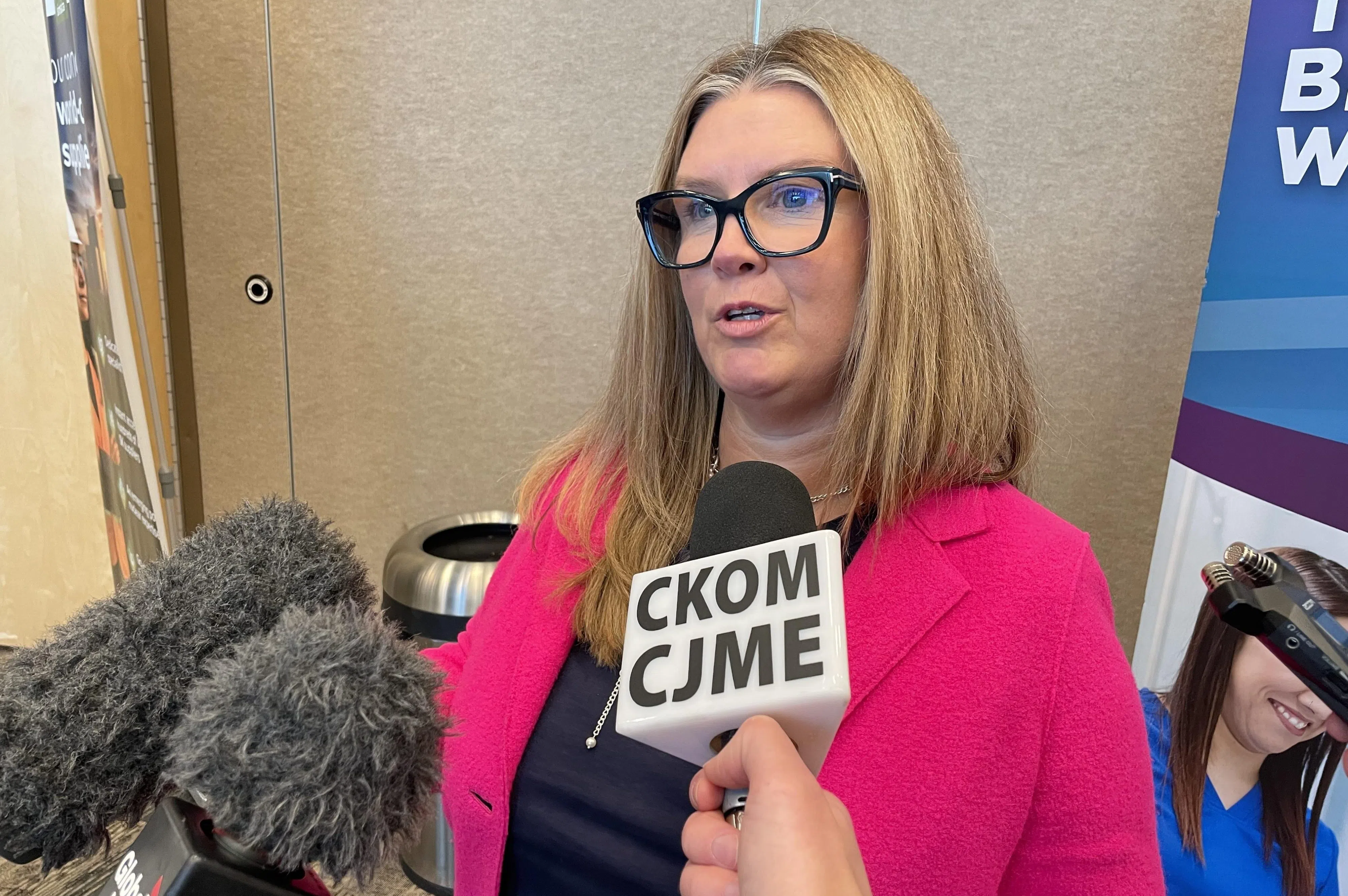 Austin looks towards reporters while wearing thick-framed black glasses and a hot pink blazer