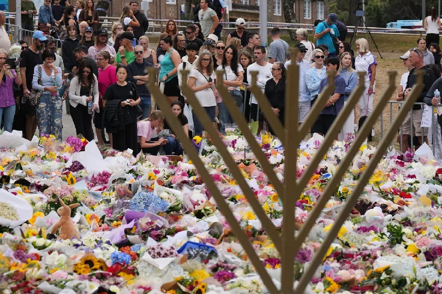 A Hanukkah menorah stands by a floral tribute as people gather to pay their respects near the Bondi Pavilion at Bondi Beach on Tuesday, Dec. 16, 2025, following Sunday's shooting in Sydney, Australia.