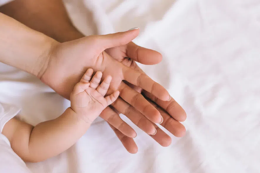 A baby and parents hold hands on a bed.