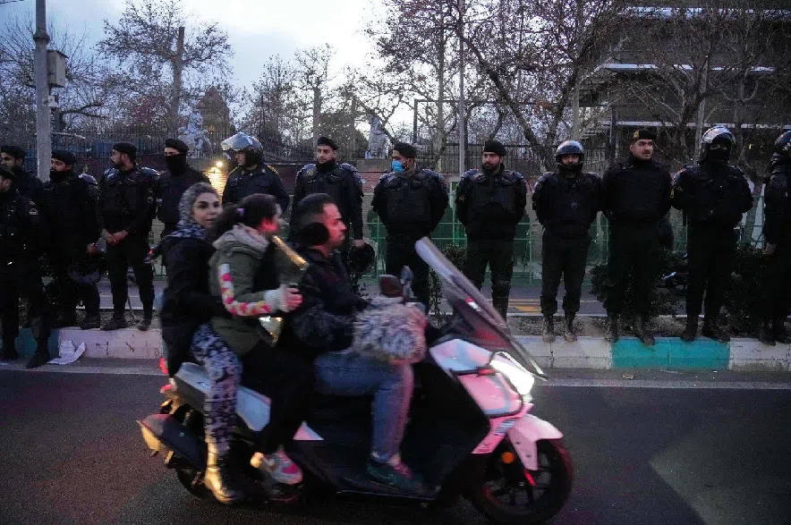 Policemen protect the British Embassy during a protest by hardline supporters of the Iranian government, as people ride on their motorbike in Tehran, Iran, Wednesday, Jan. 14, 2026.