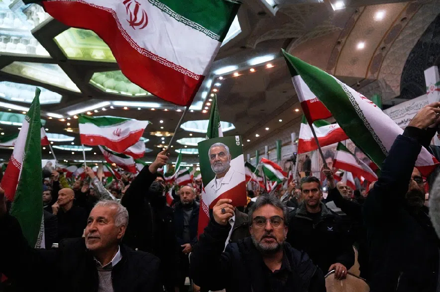 People wave Iranian flags as one of them holds up a poster of the late commander of the Iran's Revolutionary Guard expeditionary Quds Force, Gen. Qassem Soleimani, who was killed in a U.S. drone attack in 2020 in Iraq, during a ceremony commemorating his death anniversary at the Imam Khomeini grand mosque in Tehran, Iran, Thursday, Jan. 1, 2026.