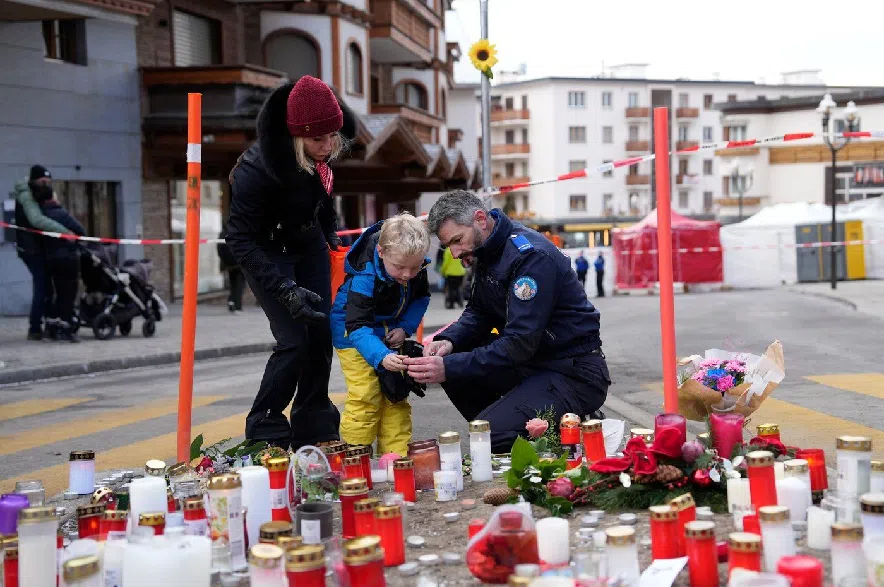 A police officer helps a boy to light a candle near the sealed off Le Constellation bar in Crans-Montana, Swiss Alps, Switzerland, Friday, Jan. 2, 2026, where a devastating fire left dead and injured during the New Year's celebrations.