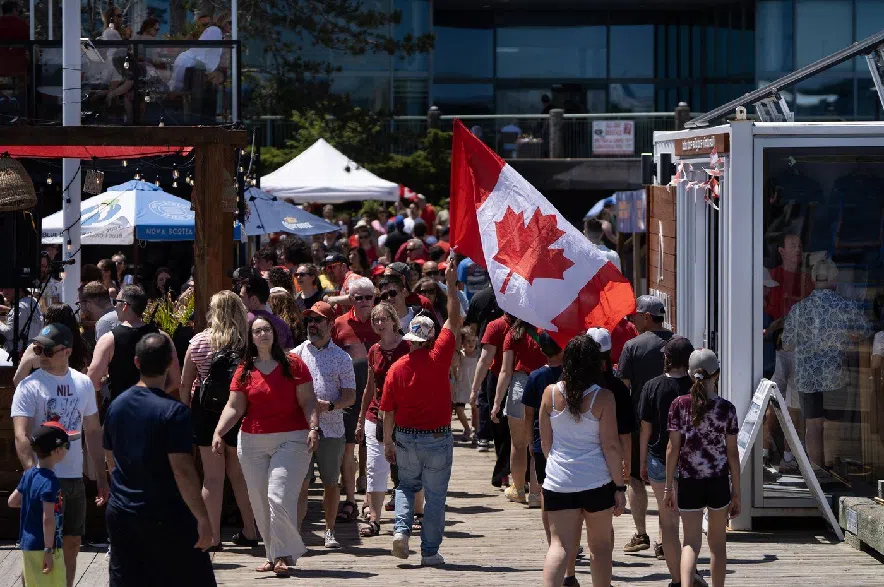 A reveller carries a Canada flag through a crowd on the Halifax Waterfront during Canada Day celebrations in Halifax, on Tuesday, July 1, 2025.