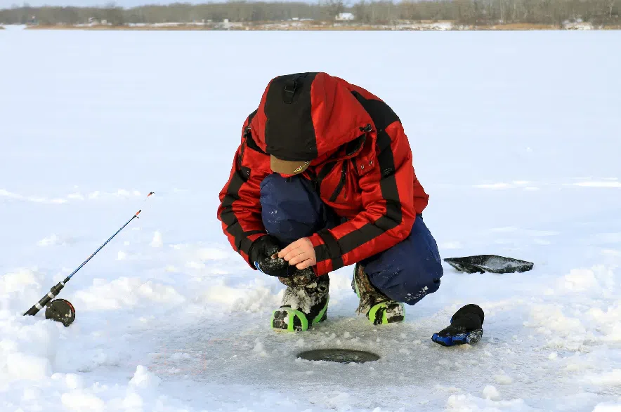 A man in a red parka ice fishing on a frozen lake.