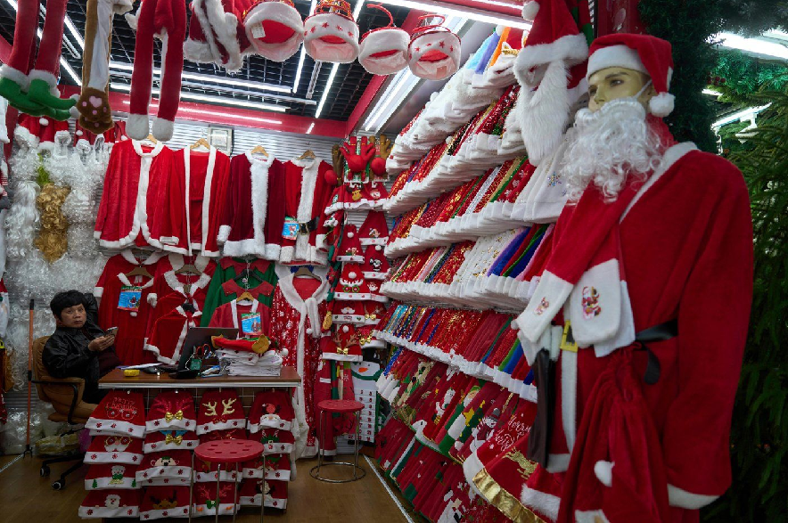 A vendor waits for customers near Santa costumes for sale at the Yiwu International Trade Market in Yiwu, eastern China's Zhejiang province on April 10, 2025.