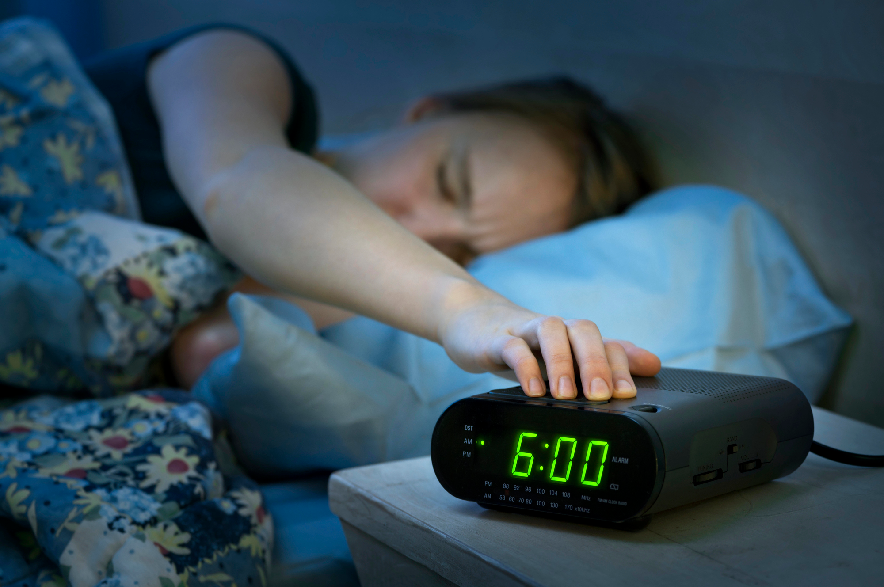 A woman pressing the snooze button on a black alarm clock.