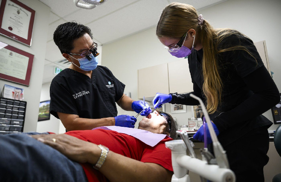 Dr. Melvin Lee, left, performs a tooth extraction for patient Robert McFarlane, who is eligible for the Canadian Dental Care Plan, as team member Sofia Christow-Filleul assists at his dental clinic in Ottawa, on Wednesday, Aug. 7, 2024.