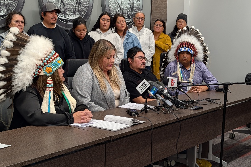 Celest Sanders (middle) speaks on behalf of Stan Moosomin (seated second from right), while flanked by Chief Tanya Stone of Mosquito Grizzly Bear’s Head Lean Man First Nation (seated left), and Chief Quenton Swiftwolfe of Moosomin First Nation at a news conference on Oct. 28, 2026. (Phil Wood/CKOM)
