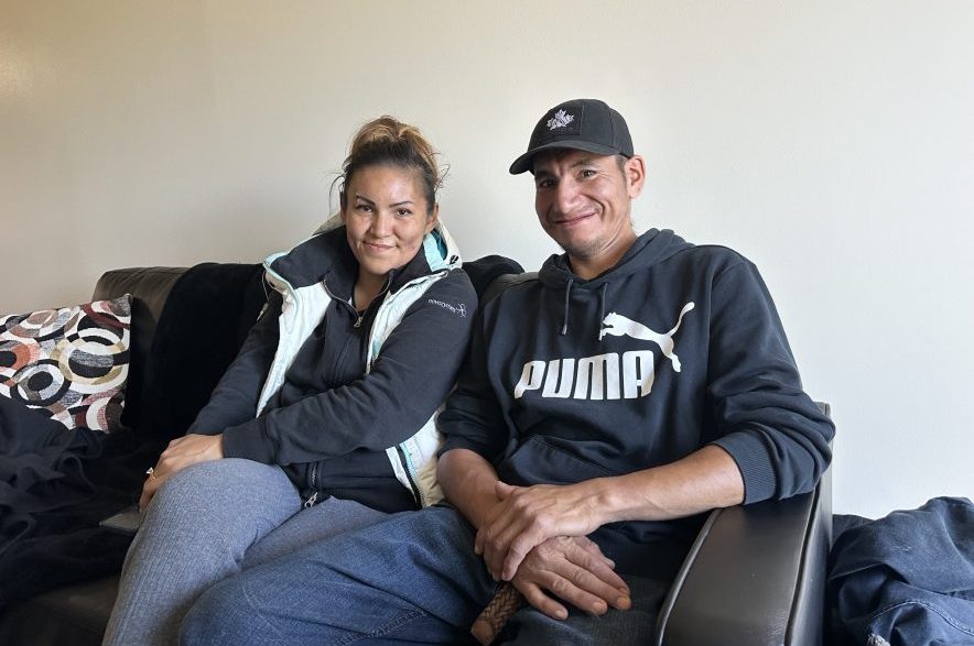 Tyler Rabbitskin (right) and Genine Okanee (left) sit on the couch in their new apartment, which came furnished. (Libby Gray/650 CKOM)
