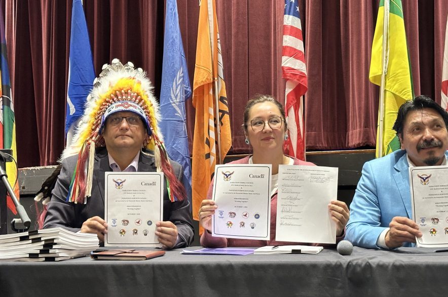 Saskatoon Tribal Council chief Mark Arcand, Minister of Indigenous Services Canada Mandy Gull-Masty and Whitecap Dakota Nation chief Darcy Bear hold up signed regional agreements at Dakota Dunes on Oct. 7, 2026. (Libby Gray/650 CKOM)