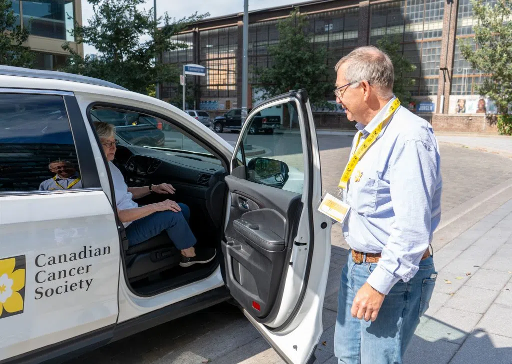 A man opening the passenger door of the Canadian Cancer Society branded car for a woman.